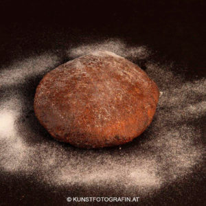 Hausgemachtes Sauerteigbrot auf mit Mehl eingestäubter schwarzer Platte (© Kunstfotografin.at)