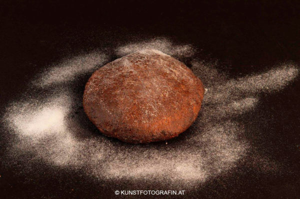 Hausgemachtes Sauerteigbrot auf mit Mehl eingestäubter schwarzer Platte (© Kunstfotografin.at)